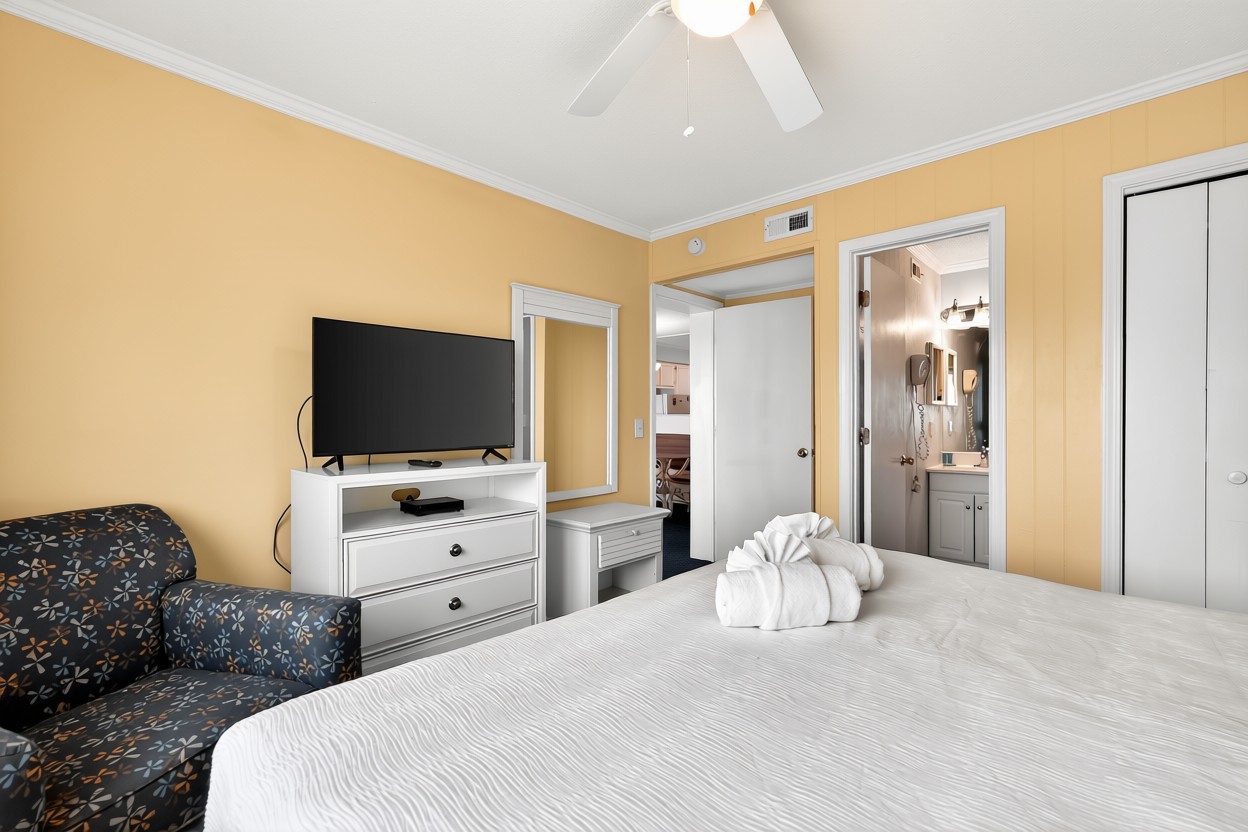 A hotel room with yellow walls, a white bed, and a TV on a stand.