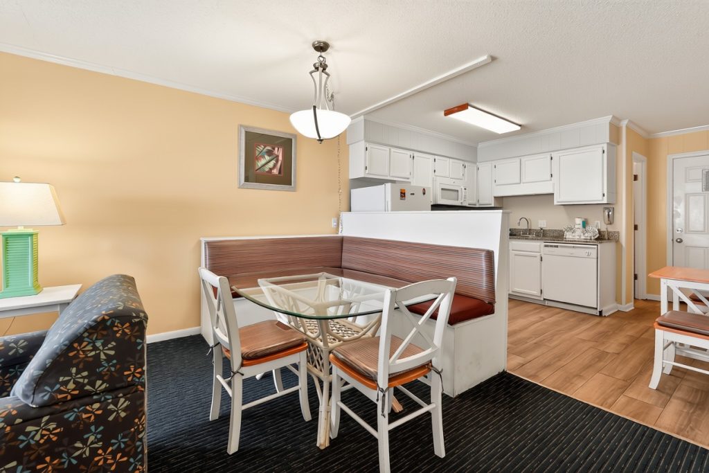A wide view of a hotel room with a kitchenette, dining area, and living room.
