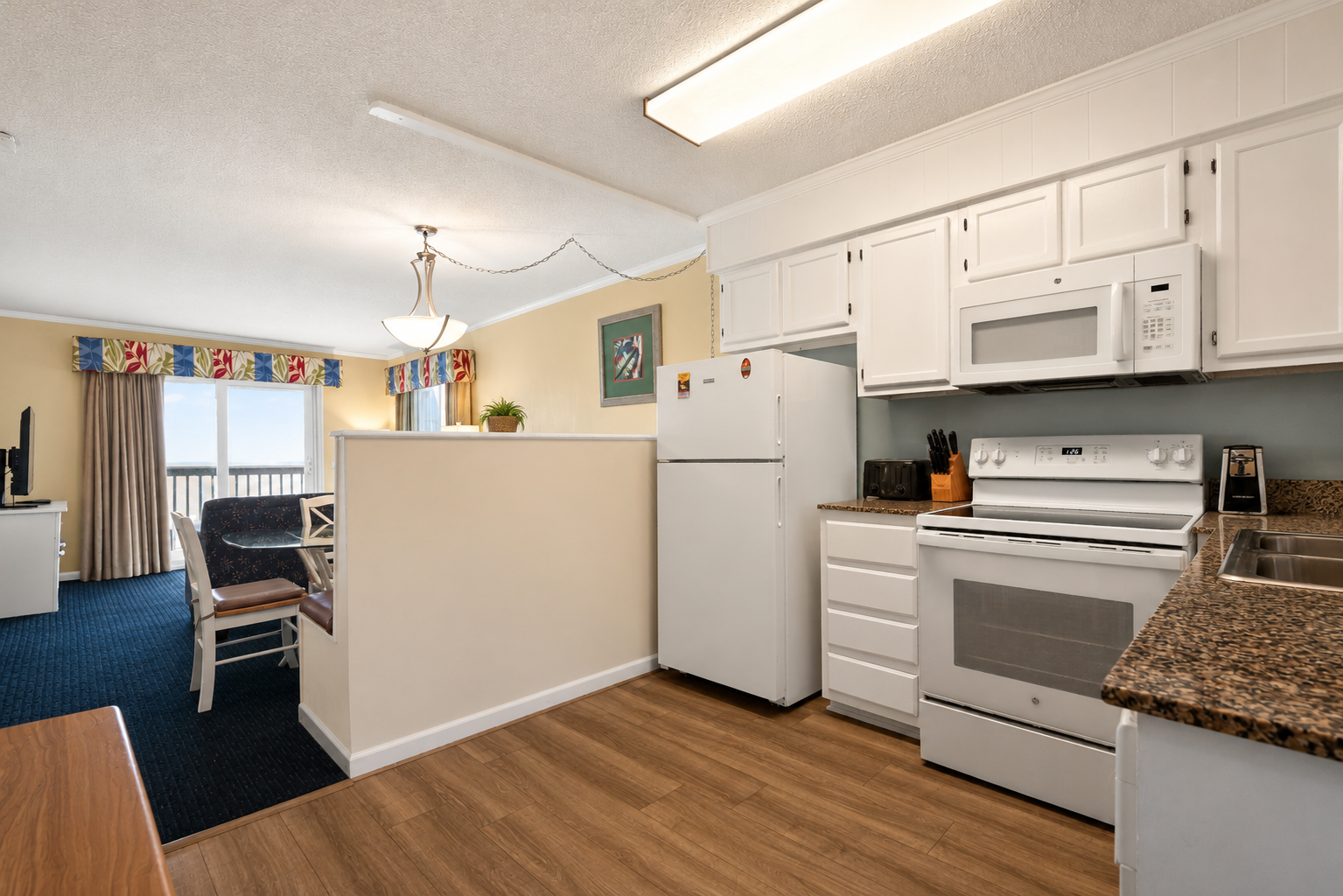 A kitchen with white appliances, granite countertops, and a dining area with a balcony